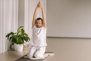 un' uomo nel bianca abbigliamento sportivo è fare yoga con un' fitness camera. il concetto di un' salutare stile di vita foto