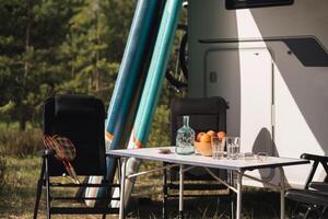 un' tavolo con piatti e sedie vicino il camper. picnic nel natura foto