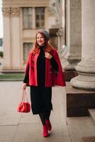 un' bellissimo elegante donna vestito nel un elegante rosso cappotto con un' elegante rosso borsetta nel il autunno città foto