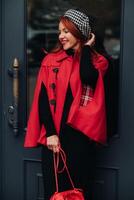 un' bellissimo elegante donna vestito nel un elegante rosso cappotto con un' elegante rosso borsetta nel il autunno città foto