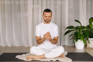 un' uomo nel bianca abbigliamento sportivo è fare yoga con un' fitness camera. il concetto di un' salutare stile di vita foto