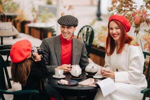 un' elegante famiglia di tre è seduta a un' tavolo al di fuori nel un' bar e potabile caffè. papà, mamma e figlia nel il autunno città foto