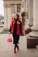 un' bellissimo elegante donna vestito nel un elegante rosso cappotto con un' elegante rosso borsetta nel il autunno città foto