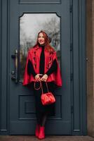 un' bellissimo elegante donna vestito nel un elegante rosso cappotto con un' elegante rosso borsetta nel il autunno città foto