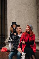 un' elegante famiglia di tre passeggiate attraverso il autunno città in posa per un' fotografo . papà, mamma e figlia nel il autunno città foto