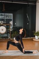 un' ragazza nel un' nero gli sport uniforme fa yoga in piedi su un' stuoia nel il Palestra foto