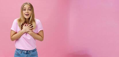 interno tiro di toccato sorpreso bella vista simpatico ragazza nel maglietta e jeans Tenere palme su cuore ansimando a partire dal divertimento e stupore reagendo per eccezionale piacevole notizia grato e contento foto