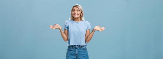 oops io fare non sapere. sciocco carino europeo ragazza con giusto capelli e freddo tatuaggi alzando le spalle con palme diffusione a parte nel no idea gesto sorridente con spiacente Guarda essere ignaro e all'oscuro al di sopra di blu parete foto