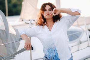 un' contento donna con lungo capelli sta su il molo vicino il yacht foto