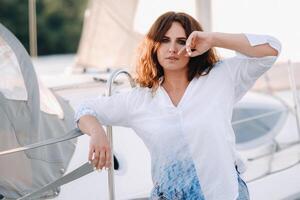 un' contento donna con lungo capelli sta su il molo vicino il yacht foto