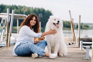 un' contento donna con un' grande bianca cane bugie su un' molo vicino il mare a tramonto foto