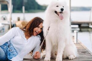 un' contento donna con un' grande bianca cane bugie su un' molo vicino il mare a tramonto foto