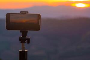 un' smartphone è registrazione il sole ambientazione al di sopra di un' montagna gamma. foto