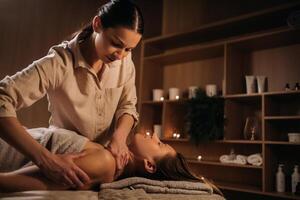 un' massaggiatrice dà un' corpo massaggio per un' donna nel un' terme centro. un' professionale massaggiatore massaggi il spalla di un' ragazza dire bugie nel un' terme centro foto