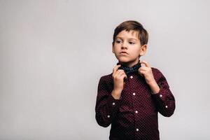 un' bellissimo ragazzo nel un' camicia e arco cravatta sta su un' grigio sfondo foto