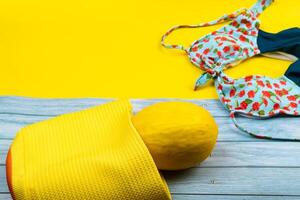 superiore Visualizza di un' costume da bagno e un' melone nel un' Borsa, dire bugie su un' blu di legno e giallo sfondo.estate vacanza concetto foto