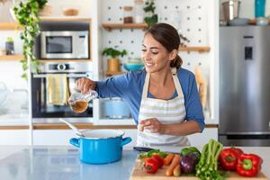 contento giovane donna cucinando degustazione cena nel un' pentola in piedi nel moderno cucina a casa. casalinga preparazione salutare cibo sorridente . domestico e nutrizione. dieta ricette concetto foto