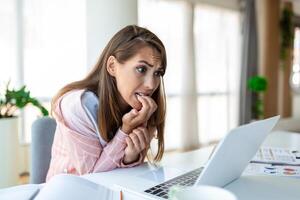 giovane donna pungente sua Chiodi mentre Lavorando su un' il computer portatile a casa. ansioso donna Lavorando nel ufficio pungente sua dita e chiodo. foto