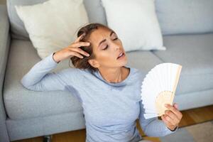 donna mette testa su divano cuscini si sente lento dovuto insopportabile calore, onde mano fan freddo se stessa, caldo estate piatto senza condizionatore clima controllo sistema concetto foto