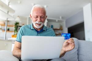 maturo uomo utilizzando computer portatile, Tenere plastica credito o addebito carta, anziano grigio dai capelli cliente fabbricazione sicuro Internet pagamento, shopping o navigazione in linea bancario servizio, entrata informazione foto