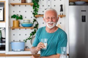 anziano uomo potabile un' bicchiere di latte con un' contento viso in piedi e sorridente. bello anziano uomo potabile un' bicchiere di fresco latte nel il cucina foto