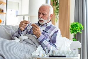 malato anziano uomo controllo il suo temperatura sofferenza a partire dal di stagione influenza o freddo dire bugie su divano tosse sofferenza a partire dal di stagione influenza o freddo. . malato anziano sentire malsano con influenza a casa foto