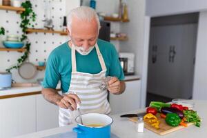 contento anziano uomo avendo divertimento cucinando a casa - anziano persona preparazione Salute pranzo nel moderno cucina - pensionato stile di vita tempo e cibo nutrizione concetto foto