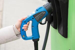 giovane donna ricarica sua elettrico auto a un' ricarica stazione nel il città. eco carburante concetto. il concetto di l'ambiente amichevole trasporto. ricarica batteria a partire dal ricarica stazione. foto