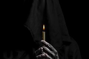 giovane cattolico suora è Tenere candela nel sua mani. messa a fuoco su candela. viso è sfocato. foto su nero sfondo.