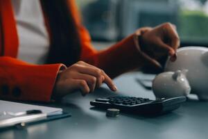 un' giovane ragazza lavori a un' computer portatile, scrive un' attività commerciale sviluppo Piano nel un' taccuino, si sviluppa un' strategia e fa calcoli di guadagnato fondi. un' donna mette sua risparmi nel un' porcellino banca. foto