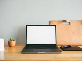 laptop e alcuni strumenti fissi sulla scrivania in legno con parete grigia vuota come sfondo. concetto di spazio di lavoro e ufficio minimo.