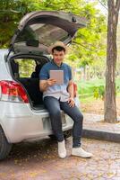 asiatico uomo seduta indietro di auto e Tenere tavoli dai un'occhiata Posizione e trova posto per viaggio. contento strada viaggio e vacanza nel estate nel il campagna. concetto di viaggio su tempo libero, strada viaggio vacanza foto