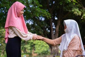 musulmano attento badante o infermiera assunzione cura di il paziente nel il ospedale parco. contento musulmano madre nel hijab abbracciare figlia. concetto di risparmi e anziano Salute assicurazione, un' contento famiglia foto