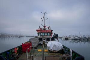 barca o nave con opera attrezzatura per pesca o ricerca - nuvoloso e nebbioso tempo metereologico nel il cantiere navale su il mare foto