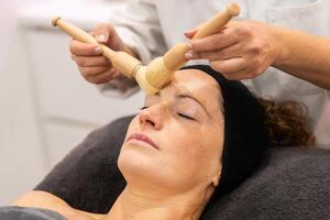 Ritaglia professionale cosmetologo pulizia viso di femmina cliente con spazzole nel bellezza salone foto