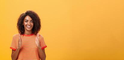 ritratto di affascinante dall'aspetto amichevole africano americano donna con afro acconciatura spiegando storia con mani e gesti modellare oggetto, Tenere palme verticale al di sopra di il petto e sorridente a telecamera foto