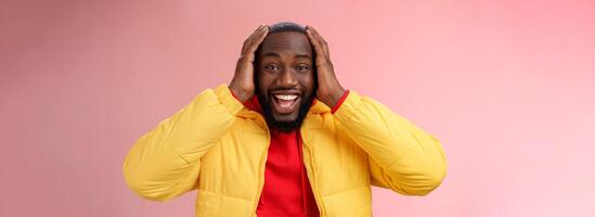 contento sorpreso lieta giovane afroamericano 25s uomo giovane giacca rosso felpa con cappuccio sorridente divertito, stupito sorridente ricevente eccezionale regalo Tenere mani testa entusiasta, in piedi rosa sfondo foto