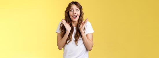 sorpreso contento lieta impressionato dai capelli ricci ragazza sguardo telecamera ammirazione soddisfazione gioia applaudire mani allegro sorridente a grandi linee Guarda telecamera affascinato entusiasta applausi giallo sfondo foto