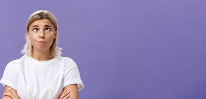 mente andando pazzo. ritratto di divertente stanco attraente giovane donna con giusto capelli e abbronzato pelle strabismo rotolamento occhi a parte e guardare su Ingannare in giro al di sopra di viola sfondo a partire dal la noia foto