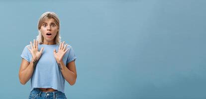 scioccato e preoccupato ha riguardato bella vista femminile donna con biondo capelli e tatuato braccia raccolta palme ansimando e apertura bocca esprimendo empatia e sensazione spiacente per amico al di sopra di blu parete foto