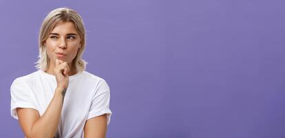 dalla vita in su tiro di inteligente creativo giovane ambizioso donna con biondo taglio di capelli e abbronzato pelle strabismo e sorridendo guardando sinistra mentre Tenere mano su mento pensiero fabbricazione su Piano o decisione foto