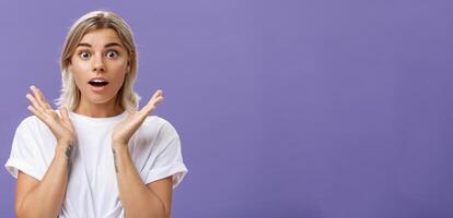 avvicinamento tiro di Ammaliato e impressionato bella vista caucasico fidanzata con biondo capelli e tatuaggi su braccia raccolta mani nel stupito e eccitato gesto apertura bocca e guardando ipnotizzato a telecamera foto