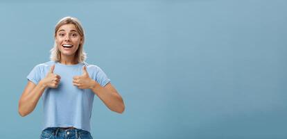 voi fatto grande orgoglioso di voi. ritratto di soddisfatto e affascinato attraente contento fidanzata nel casuale maglietta mostrando pollici su e sorridente a grandi linee essere supporto e allegro al di sopra di blu parete foto