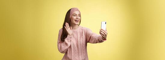 affascinante estroverso fidanzata avendo in linea video Chiacchierare, Tenere smartphone agitando a Telefono telecamera detto Ciao parlando attraverso video chiamata sorridente amichevole durante piacevole conversazione, registrazione saluto foto