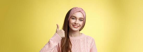 bella europeo giovane ragazza nel fascia per capelli, rosa maglione sorridente incantato, lieta mostrando pollici su nel accordo, approvazione, dando bene raccomandazione, simpatia interessante grande idea sorridente allegro foto