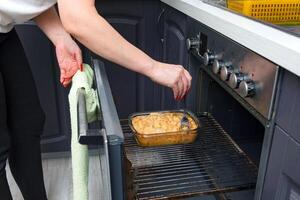 vicino su di un' donna di mani cucinando un' torta nel il forno. foto