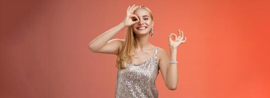 affascinante divertente tenero femminile biondo fidanzata danza avendo divertimento godendo Perfetto festa sorridente a grandi linee mostrare va bene ok eccellente gesto piace nuovo vestito ghignante soddisfacente, rosso sfondo foto