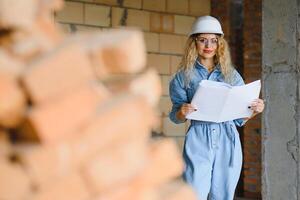 costruzione concetto. bella femmina costruttore nel tuta da lavoro e casco Lavorando su costruzione luogo. foto