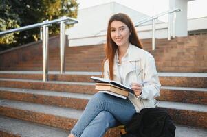 femmina Università alunno con libri all'aperto. sorridente scuola ragazza con libri in piedi a città universitaria. io sono preparato per esame molto bene. ritratto di Perfetto alunno a il Università foto