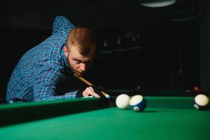 giovane bello uomo pendente al di sopra di il tavolo mentre giocando snooker foto